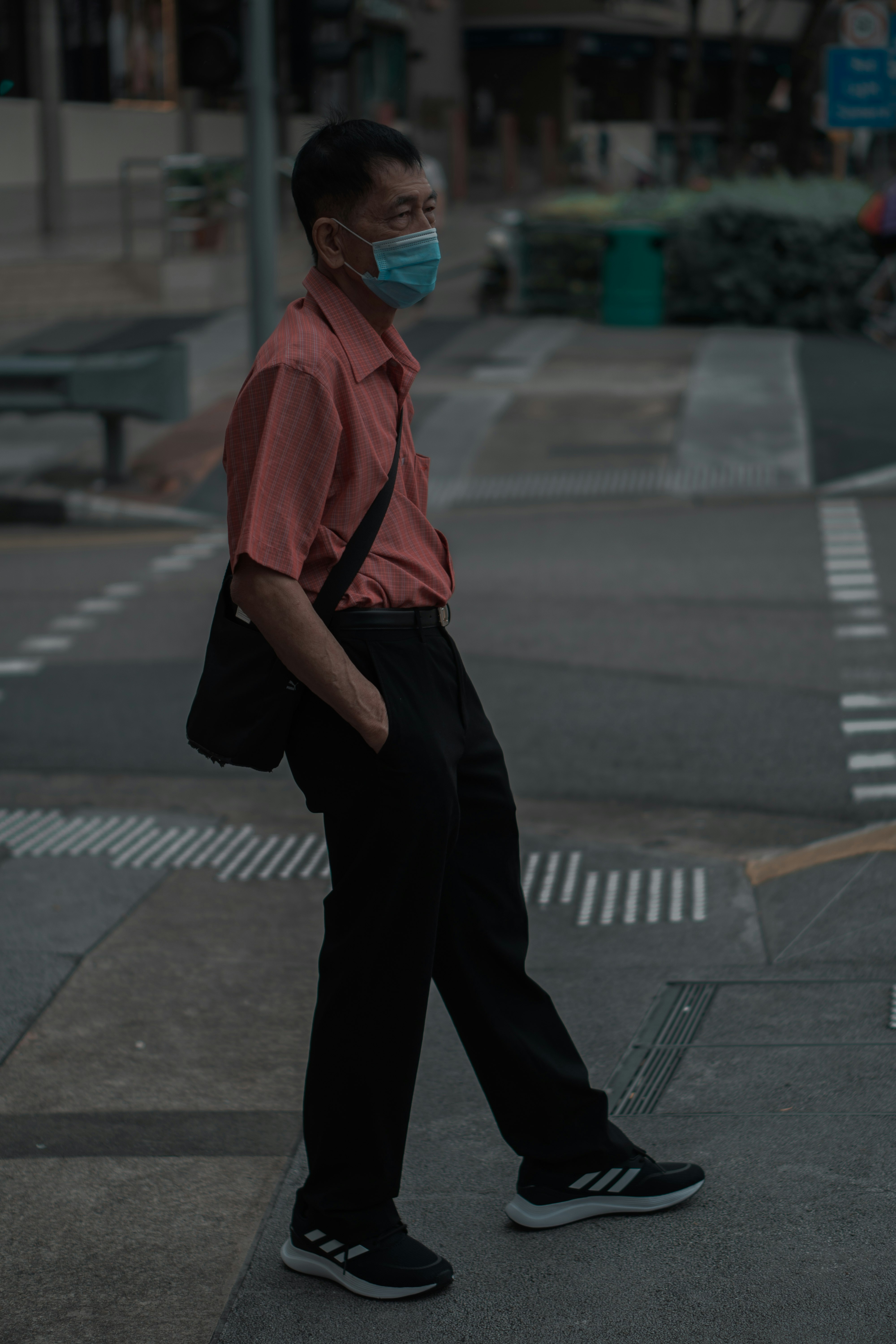 man in orange hoodie and black pants standing on sidewalk during daytime